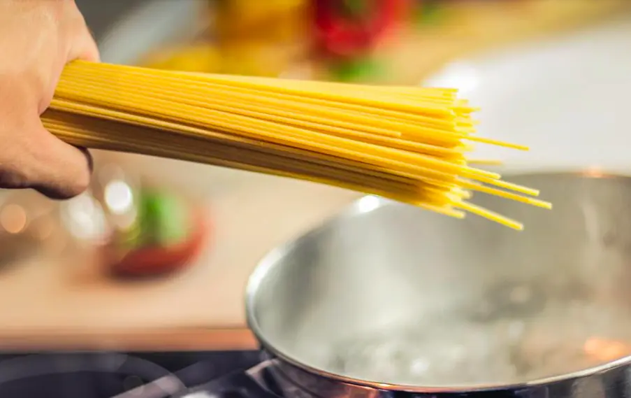 how to boil spaghetti-a hand about to put spaghetti in water