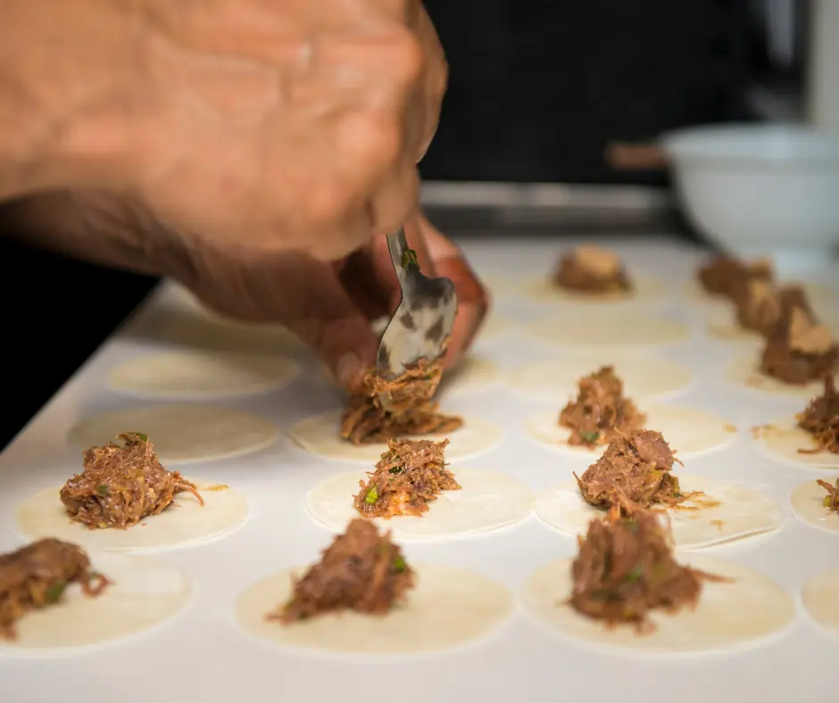 detail of two hands pouring the typical agnolotti meat filling onto some already cut pieces of pasta