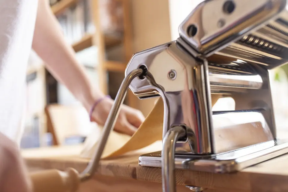 a pasta machine on a table, in the process of being used to make a ravioli pasta sheet