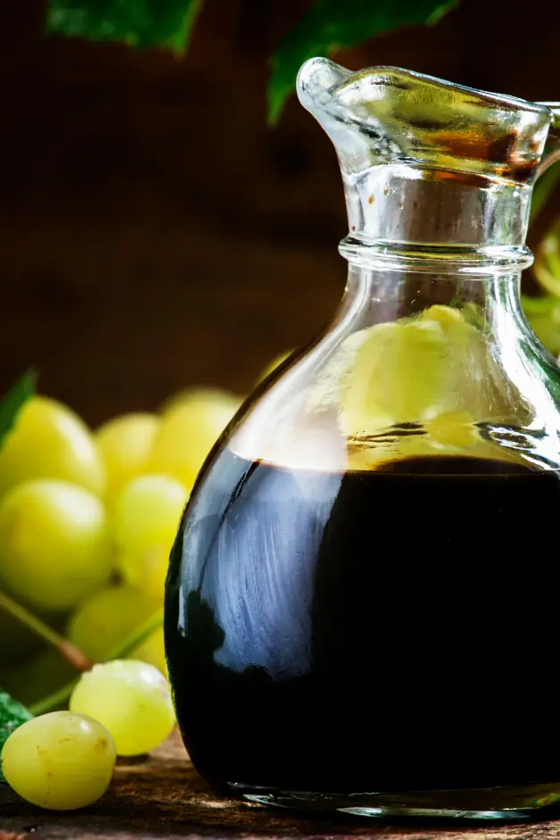 italian sausage in oven-balsamic vinegar in a small glass carafe with some grapes in the background