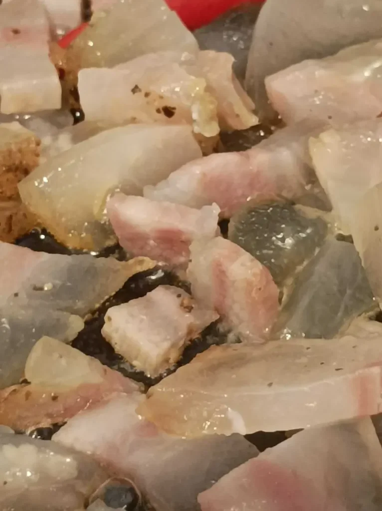 pieces of guanciale sauteeing in an iron pan