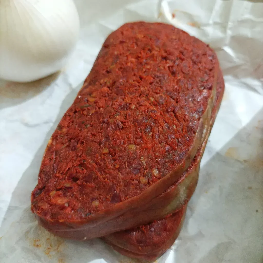 3 slices of 'nduja on a paper wrap, aside an onion