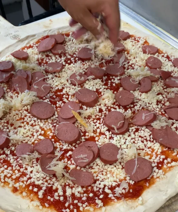 a hand distributing grated pecorino cheese over a german pizza right before tossing it in the oven.