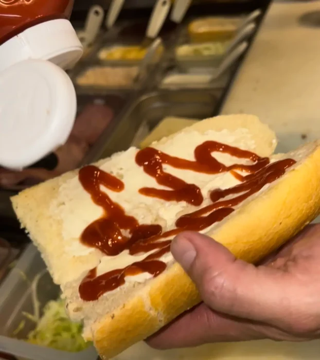 chopped cheese sandwich-adding sauces to a hoagie roll