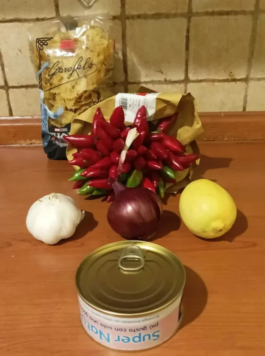 the ingredients for this spicy tuna pasta recipe on a table: canned tuna, garlic, an onion, a lemon, and a bunch of chili peppers
