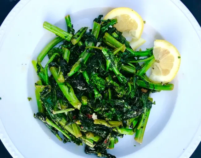 sauteed rapini on a plate with lemon wedges