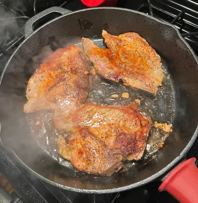 Pan seared pork chops cooking in a cast iron skillet