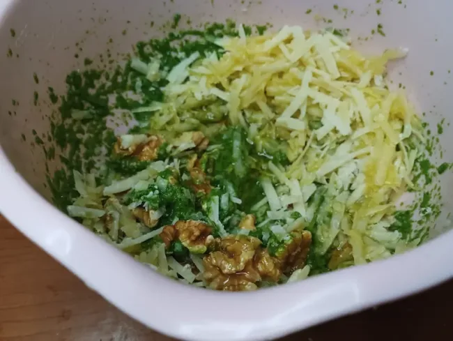mixing the ingredients for pesto in a bowl with a blender 