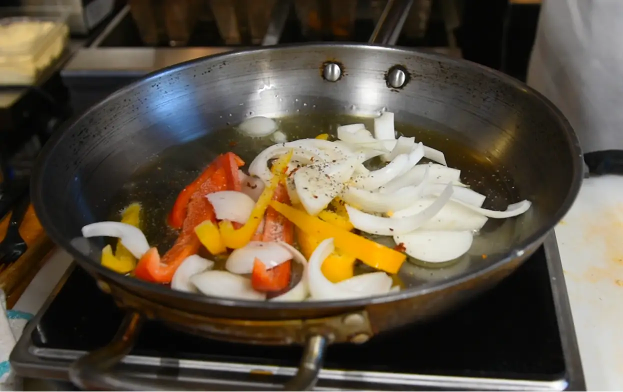 Italian sausage cooking with sliced bell peppers and onions